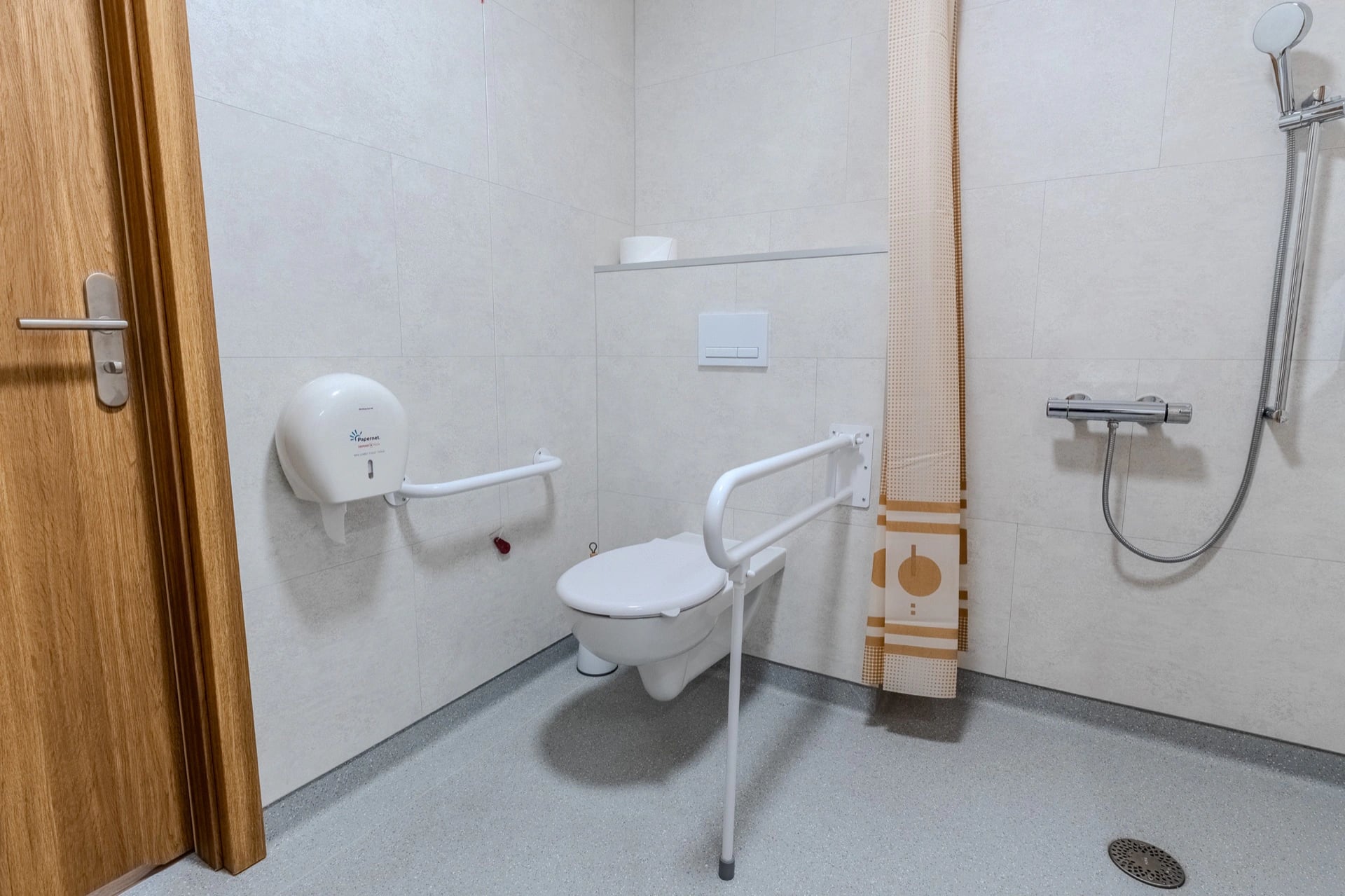 Łazienka z prysznicem bez brodzika i składanym uchwytem przy WC