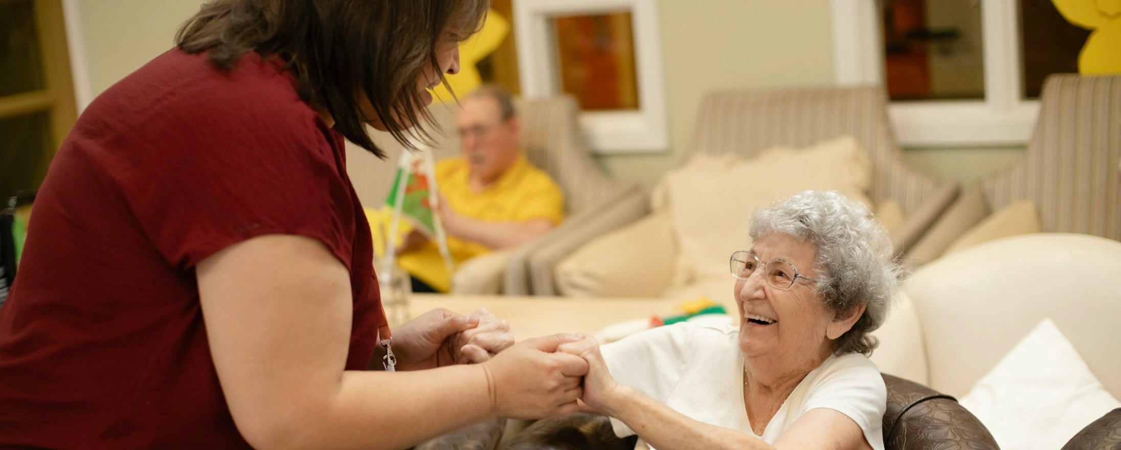 Opiekunka trzyma za ręce uśmiechniętą seniorkę