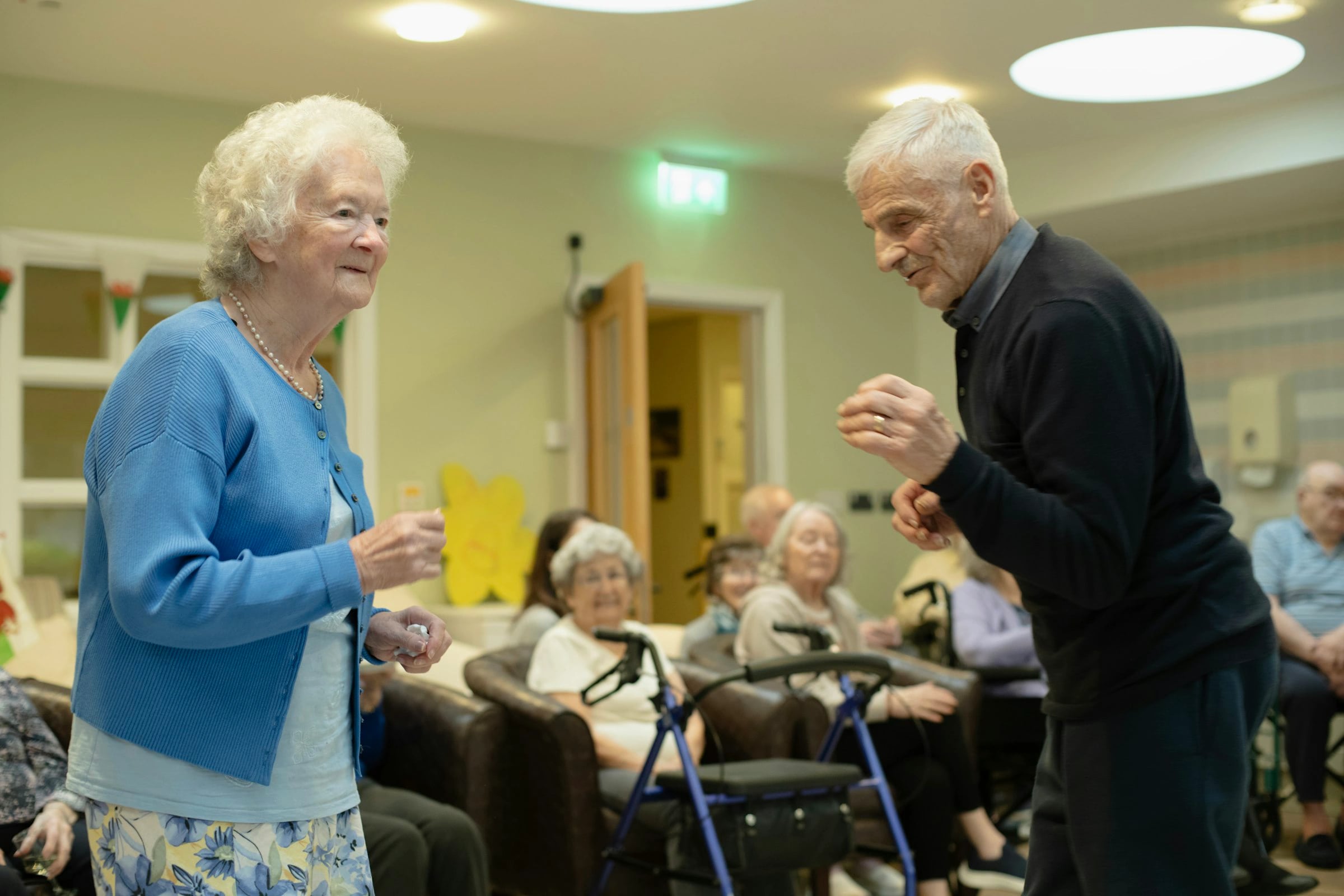 Seniorzy tańczą we wspólnej sali, pozostali mieszkańcy patrzą z uśmiechem